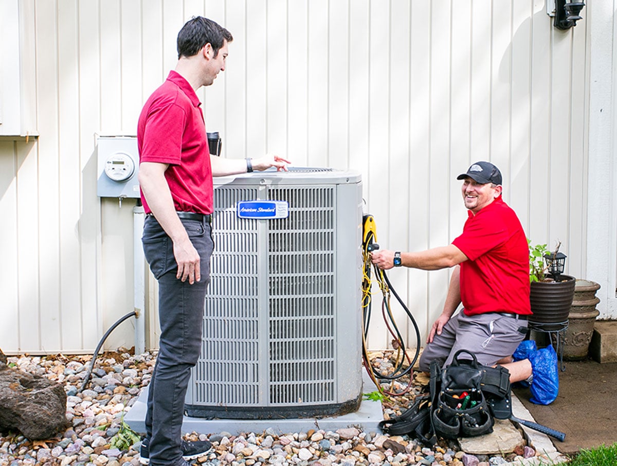 Two air conditioning repair technicians working on a home's AC unit. Two air conditioning repair technicians working on a home's AC unit.